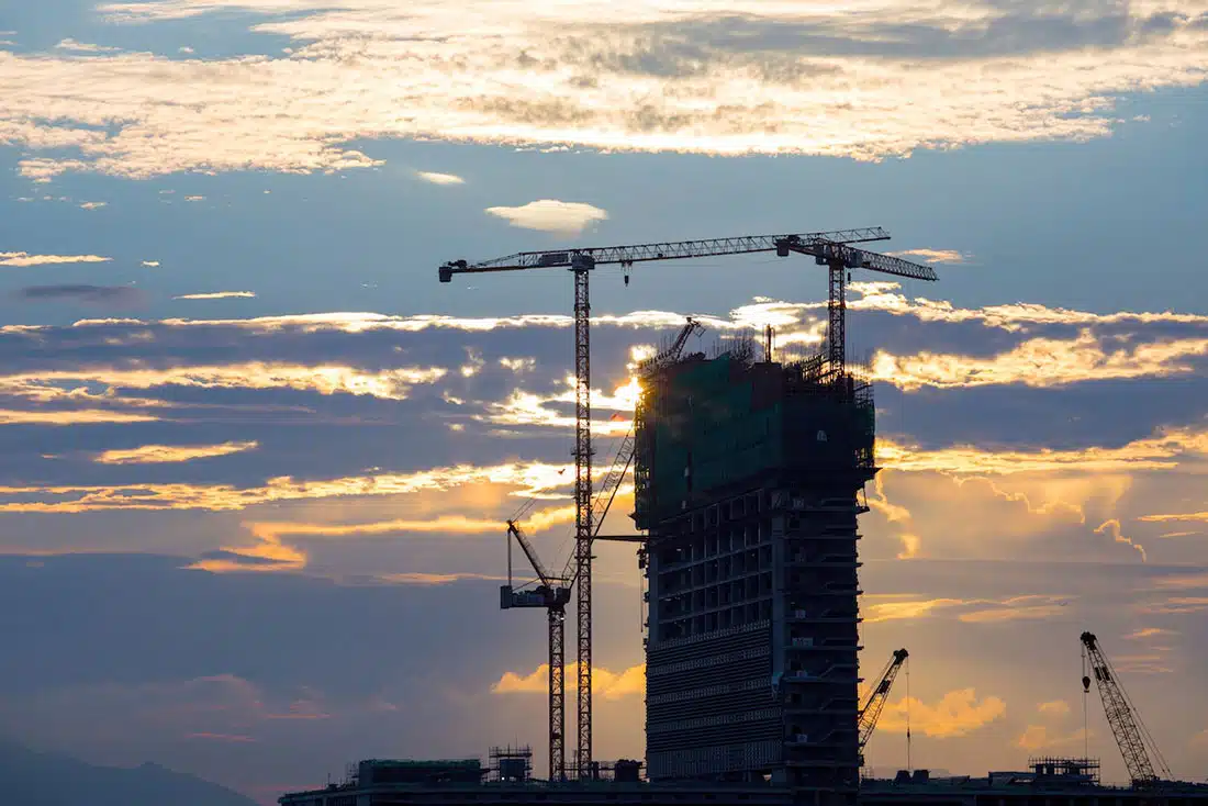 A tower building under construction at sunset. A silhouette of the building with cranes around it