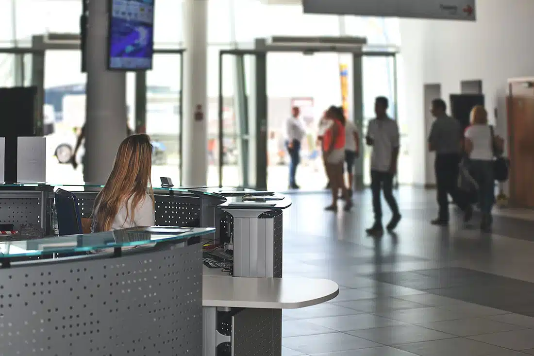 The ground floor of an office building. To the left, there’s a receptionist in focus, to the right, blurred occupants