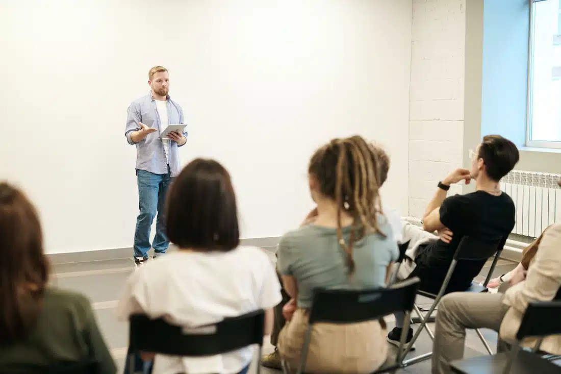 A man hosting an employee training session in front of a blurred room for people.