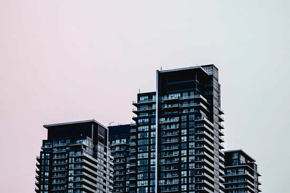 The top levels of a grey apartment building against a pink and blue hazy sky