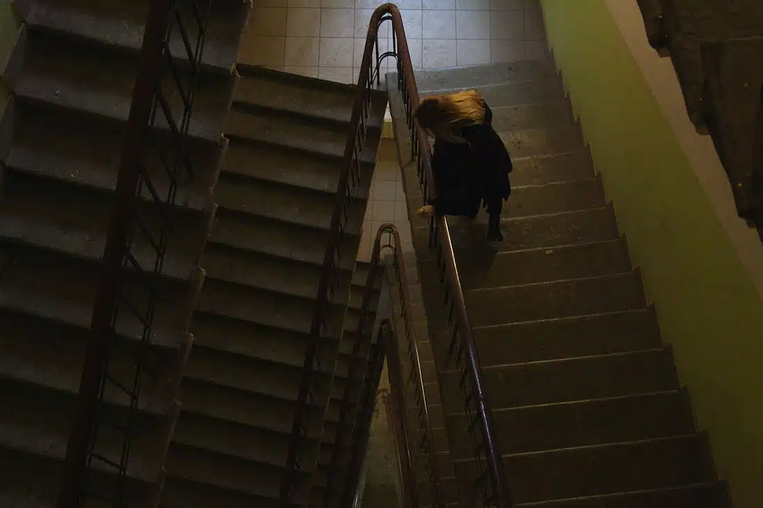 A dark photo of a woman looking down from the landing of a stairwell at the many flights below.