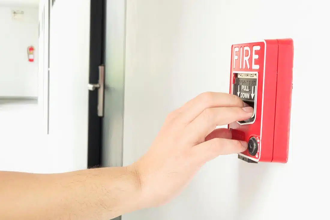 A close-up of a hand pulling down a fire alarm switch in a hallway, signifying an emergency scenario where rapid evacuation might be necessary. This image highlights the relevance of accessible evacuation equipment, such as evacuation chairs, in emergency preparedness for aging individuals.